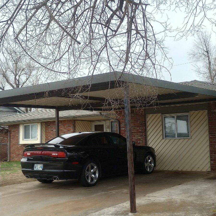 Heavy, dead overhanging branches drooping low over the same carport before removal